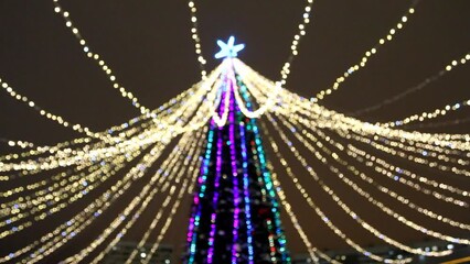 Wall Mural - Blurred Christmas tree with multi-colored and golden bokeh lights of garland at night