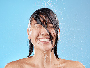 Canvas Print - Shower, woman and water with a face cleaning for clean, wash and hygiene on a blue studio background. Bathroom, showering and asian female cleansing her body for health and wellness in studio