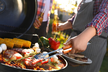 Man with drink cooking meat and vegetables on barbecue grill outdoors, closeup