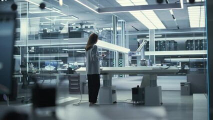 Poster - Industrial Robotics Engineer Comes to a Table With Robotic Arm in a High Tech Factory. Female Scientist Uses Tablet Computer to Manipulate and Program the Robot to Pick Up and Move a Metal Component.