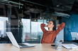 © Liubomir - Satisfied happy and successful business woman smiling and resting, hispanic female worker finished work and put her hands behind her head, dreams of victory.