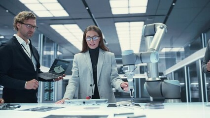Fototapete - Female Industrial Robotics Engineer Discussing the Development of a Robotic Arm Machine with Her Colleagues. Specialists with Laptop and Tablet Computers Research the Possibilities of the Robot.