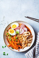 Wall Mural - Chicken ramen bowl with carrots, noodles, egg, radish and green onions, gray background. Asian cuisine concept.