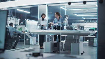 Poster - Professional Multicultural Team of Two Female Engineers Using Industrial Programmable Robotic Arm in a Factory Development Workshop. Robot Hand Machine Picking Up and Holding a Microchip.