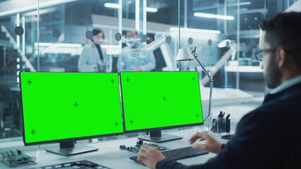 Fototapete - Robotics Engineer Working on a Desktop Computer with Two Green Screen Chromakey Display Screens in a Startup Factory. High Tech Technological Research and Development Company.