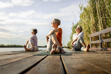 Wall Mural - Group of senior woman doing yoga exercises by the lake.