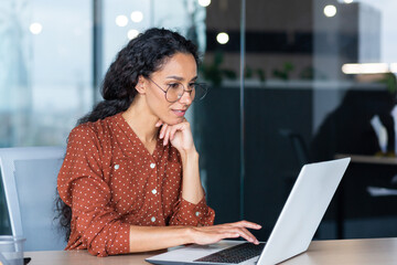 Successful Indian woman developer programmer working inside modern office, using laptop at work to write program software code, smiling and happy startup.