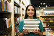 © AntonioDiaz - Hispanic woman looking happy carrying a lot of books at the bookstore