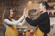 © Irin - A postitive barista, staff or waitress and waiter give high five with both hands with the successful result or target. Concept of cheerful, frienship co-worker, celebrate at coffee shop and bakery.