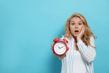 Emotional woman with alarm clock in turmoil over being late on light blue background. Space for text