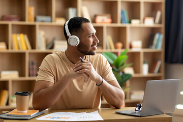 Poster - Positive pensive arab man working online at home, sitting at workdesk in front of laptop, looking aside at copy space