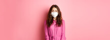 Covid-19, Pandemic And Lifestyle Concept. Excited Young Woman Wearing Respirator While Going Out, Social Distance Herself During Quarantine, Pink Background