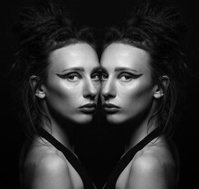 Portrait Of Beautiful Woman With Eye Shadows Make-up, Long And Dark Dreadlocks Hair Looking At Camera With Seductive Look. Same Model Reflection Effect Standing Near Each Other. Black And White Image