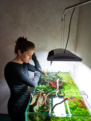 A beautiful woman stands in thoughts leaning her hands on the aquarium aquascape and looking into