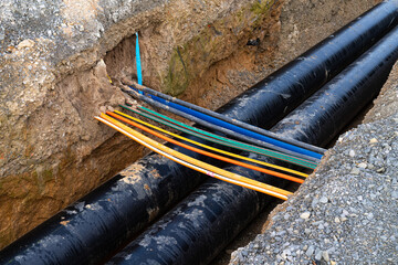 Trench with two laid heating pipes. Multicolored electrical cables cross the trench. View from above.