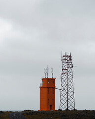 An orange light tower next to a metal radio tower, Hvalnes, Iceland.