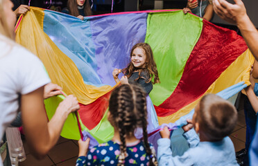 Little girl of preschool age, child dancing, spinning indoors in a competition with a long multi-colored cloth animator in honor of the birthday.