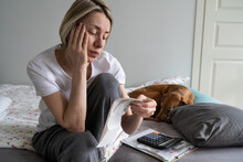 Upset Middle Aged Woman With Pay Bills And Calculator Sits On Bed With Dog In Home M Interior. Perplexed Mature Female With Financial Problems Stressed When Sees Too Much Rent Or Electricity Costs