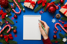 Woman writing Christmas to do list on notebook on colored background with xmas decorations