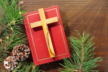Wall Mural - Wood cross laying on a closed red Christian bible with green fir branches and cones on a wooden background with copy space. Christmas holidays. Christian religion card. Flat lay