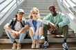 © Seventyfour - Diverse group of young people wearing street style clothes outdoors while sitting on stairs in urban area and looking at camera