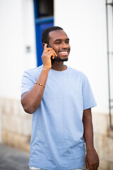 Wall Mural - Handsome young african guy walking outside talking on mobile phone and smiling