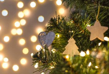 Wall Mural - Christmas tree decorated with handmade wooden toys in the shape of a star and heart on a blurry, sparkling background, close-up