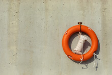 Orange Lifebuoy And White Rope Hanging On The Concrete Wall Of The Pier.