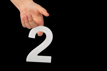 Aufkleber - Close-up hand holding a white number 2 on a black background. Number two isolate on black background in child's hand.