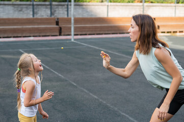 Mom and daughter have fun on the outdoor sports ground. A Caucasian woman throws candy and a girl catches it with her mouth.