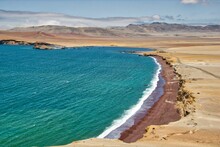 Pacific Ocean Meets The Desert In Paracas, Peru, With The Background Of Mountains And A Blue Sky