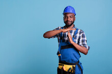 Construction Worker Making The Pause Gesture On Camera, Showing The T-shaped Stop Sign With Arms In The Studio. African American Builder Requesting Time Out For A Short Break, Wearing Hard Hat And