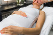 © PoppyPix - Soon-to-be mom getting spa facial treatment to relax and reduce stress in her life. Unrecognizable pregnant woman in white tank top lying on her back during gentle face-lifting massage. High quality