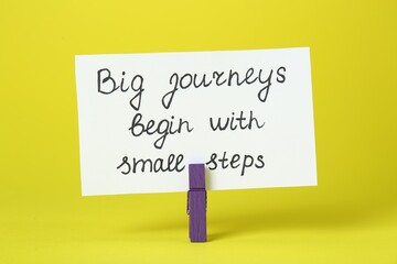 Wall Mural - Card with phrase Big Journeys Begin With Small Steps and clothespin on yellow background. Motivational quote