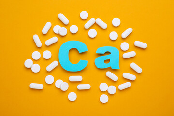 Wall Mural - Pills and calcium symbol made of light blue letters on orange background, flat lay