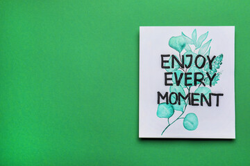 Wall Mural - Card with beautiful phrase Enjoy Every Moment on green background, top view. Space for text