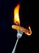 sausage on a fork in fire and black background