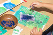 A kid works in a preschool class wit glue. Kid's hands are during creating of an art project. 
