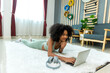 © kanpisut - Woman lying on floor and using laptop at home in living room
