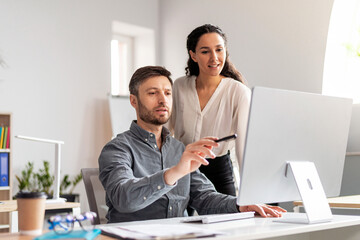 Poster - Cheerful young caucasian male manager show to lady with hand at computer in modern office interior