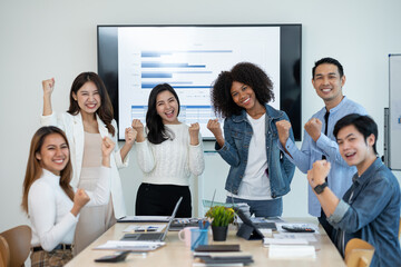 Wall Mural - Group of young Asian businessmen are happy work together as a team and achieve goals excited about the work of raising hands to congratulate colleagues in the office.