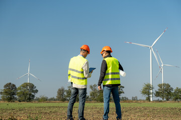 Windmills produce alternative energy in countryside. Technicians of maintenance in helmets talk about project against wind generators back view