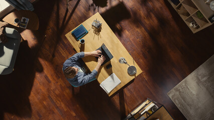 Poster - Top View Shot: Freelance Entrepreneur Sitting at Desk Opens Laptop and Starts Working. Remote Access Professional Writes Emails, Manages Social Media Corporate Campaign, Designs Software.