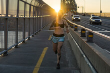 Young Tattooed Woman Running On Bridge With Sunset Behind