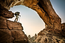 A Hiker Stands Beneath An Arch In Arches National Park, Utah.