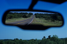 View in rear view car mirror of road through the Texas Hill Country.