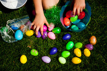 A Child Reaches For Easter Eggs In The Grass On A Farm In Iowa.