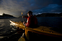 A Man Kayaks On The Waters Off Of Kalvag, Norway.
