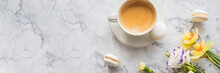 Macaroons With White Cup Of Coffee, Bright Beautiful Flowers On Marble Background.Beautiful Breakfast For Woman. Spring Concept.Copy Spaceю Web Banner