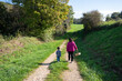 A mother holding a wicker basket and her child walking on a path in the countryside, looking for mushrooms, on a beautiful sunny day. Mother and son strolling on a footpath.
